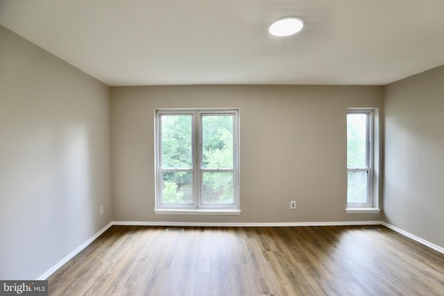 spare room featuring visible vents, baseboards, a healthy amount of sunlight, and wood finished floors