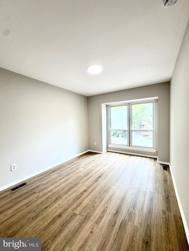 unfurnished room featuring baseboards, visible vents, and wood finished floors