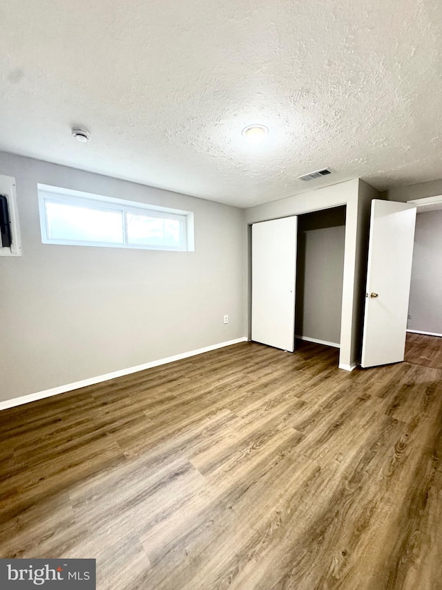 unfurnished bedroom featuring a textured ceiling, baseboards, visible vents, and wood finished floors