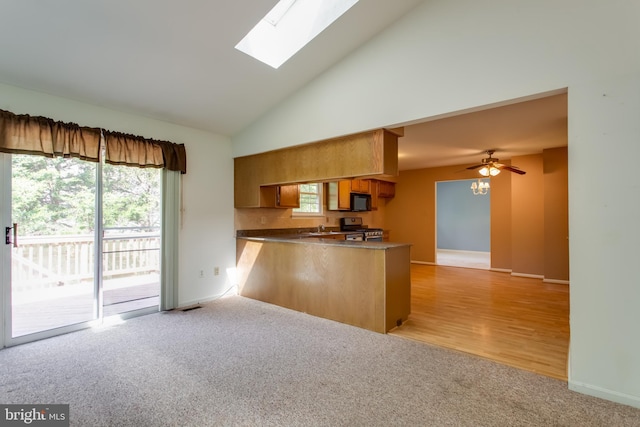 10703 Moray Ct, Cheltenham, MD 20623 - kitchen with stainless steel gas stove, a peninsula, light carpet, black microwave, and a skylight