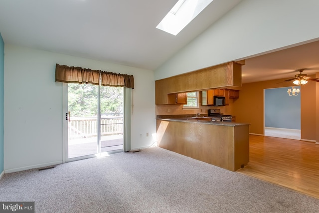 10703 Moray Ct, Cheltenham, MD 20623 - kitchen with stainless steel range with gas cooktop, a peninsula, black microwave, a skylight, and high vaulted ceiling