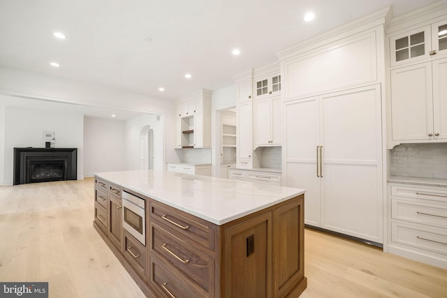 kitchen with stainless steel microwave, backsplash, light wood finished floors, white cabinets, and a center island