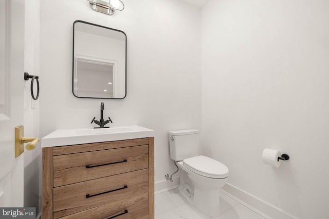 half bathroom with toilet, baseboards, vanity, and marble finish floors