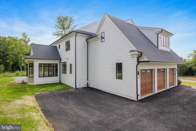rear view of property featuring driveway, roof with shingles, a garage, and a yard