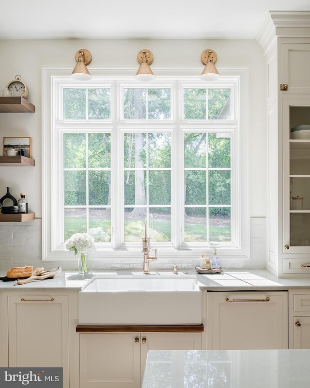 detailed view of a sink, white cabinetry, decorative backsplash, and open shelves