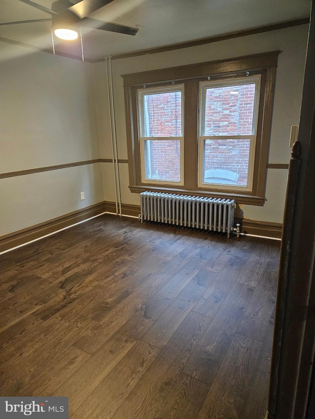 spare room featuring radiator, dark wood finished floors, ceiling fan, and baseboards