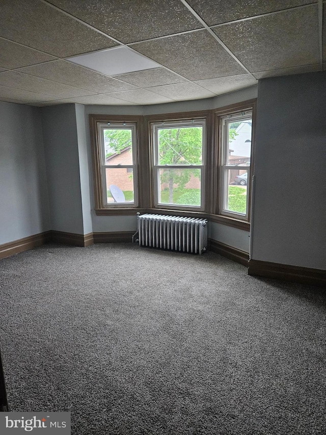 carpeted spare room featuring radiator heating unit, baseboards, a drop ceiling, and healthy amount of natural light