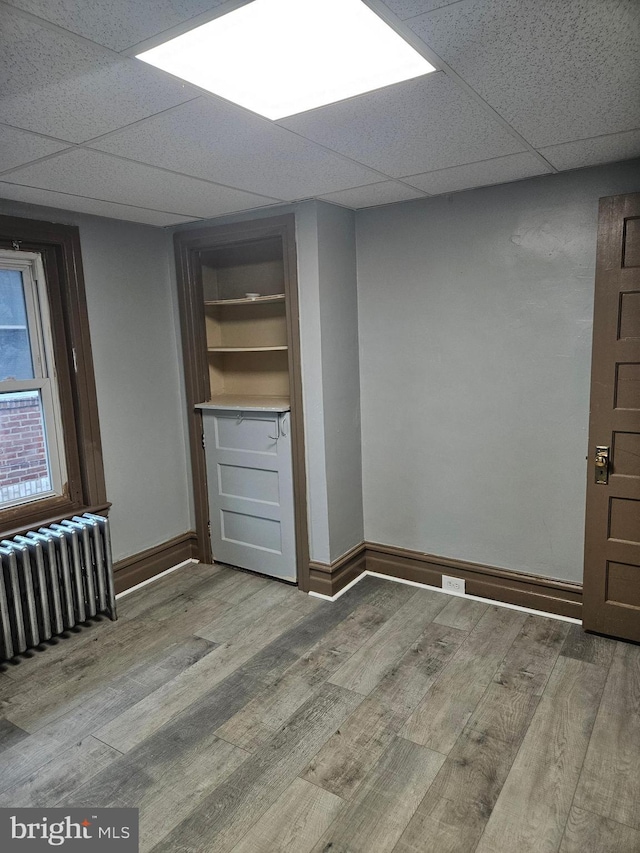 spare room featuring radiator heating unit, wood finished floors, baseboards, and a drop ceiling