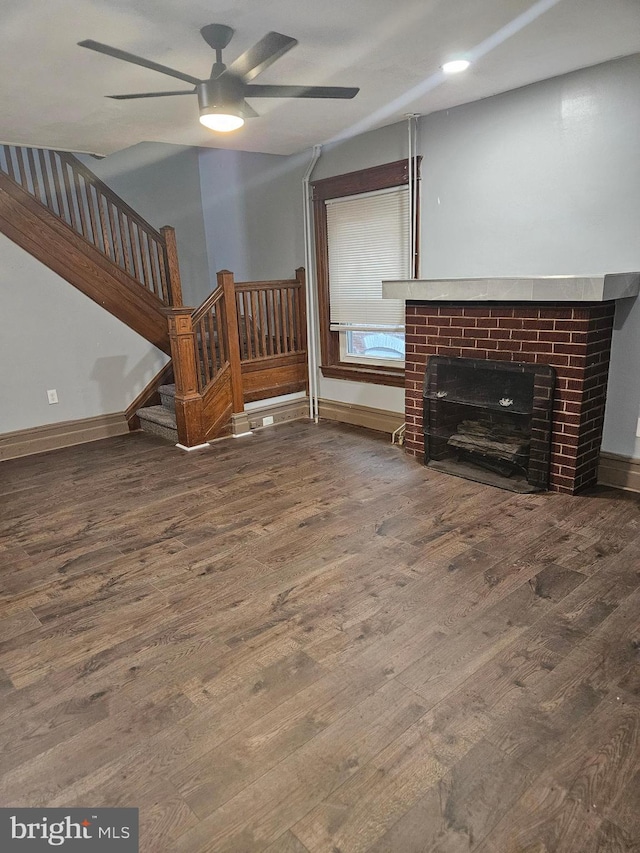 unfurnished living room with wood finished floors, a ceiling fan, a brick fireplace, and stairway