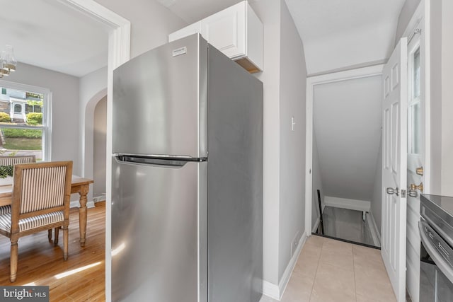 kitchen with freestanding refrigerator, baseboards, white cabinets, and arched walkways