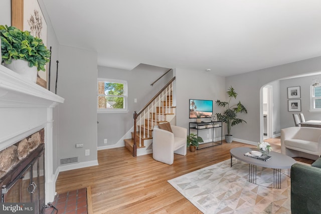 living area with stairway, visible vents, arched walkways, light wood-style floors, and a fireplace