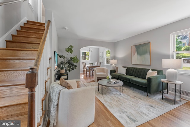 living room with arched walkways, a wealth of natural light, stairway, and wood finished floors