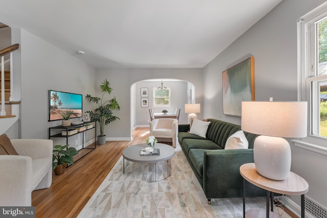 living room featuring stairs, visible vents, arched walkways, baseboards, and light wood-style floors