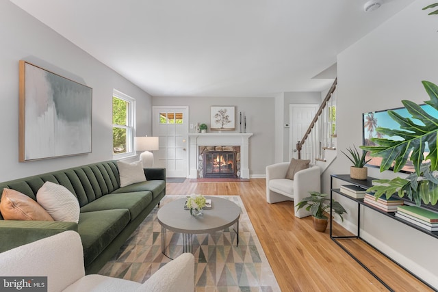 living area with stairway, baseboards, a fireplace with flush hearth, and wood finished floors