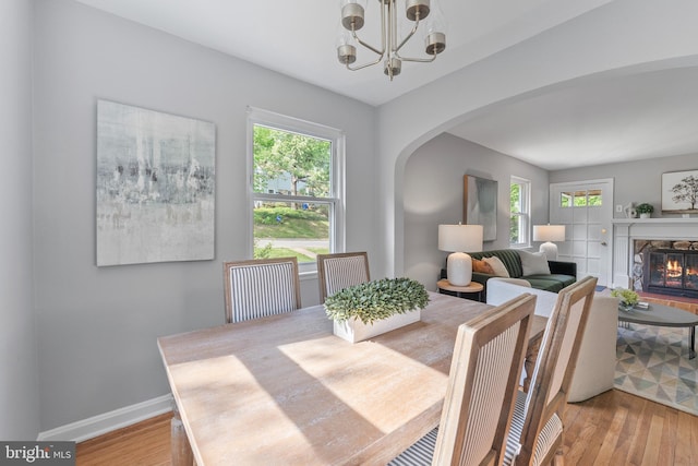 dining room with arched walkways, light wood-style floors, an inviting chandelier, and baseboards