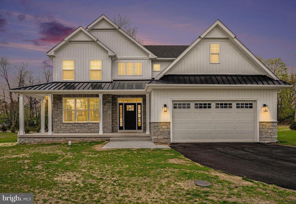 view of front of house with a standing seam roof, stone siding, driveway, covered porch, and a garage