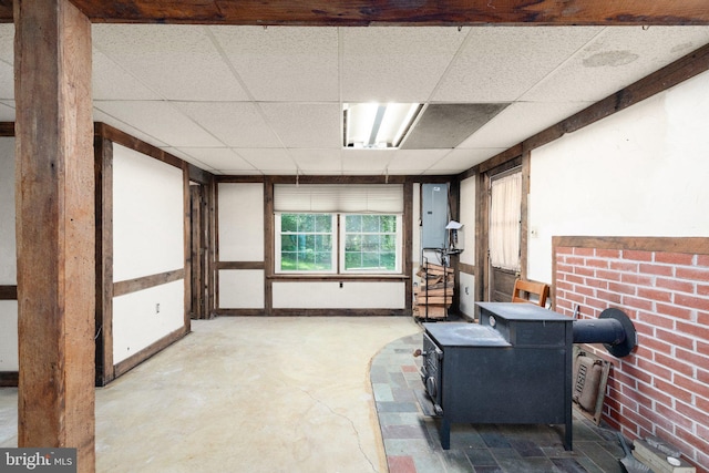 interior space with electric panel, a wood stove, and a drop ceiling