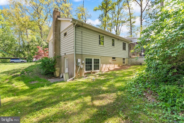 rear view of property with a chimney, a sunroom, and a lawn