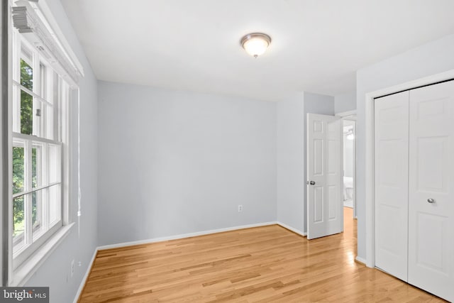 unfurnished bedroom with multiple windows, light wood finished floors, baseboards, and a closet