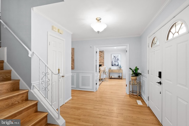 entrance foyer with stairs, light wood finished floors, ornamental molding, and a wainscoted wall