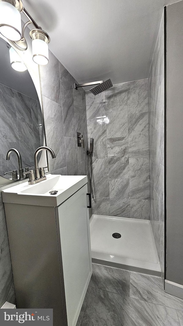 full bathroom featuring tile walls, marble finish floor, vanity, baseboards, and tiled shower