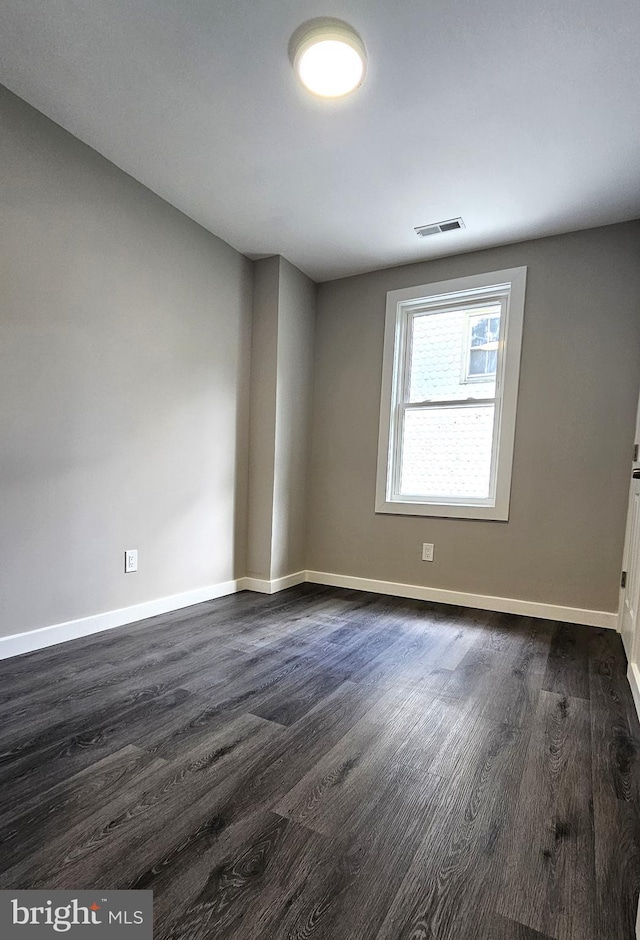 unfurnished room featuring baseboards, dark wood-style floors, and visible vents