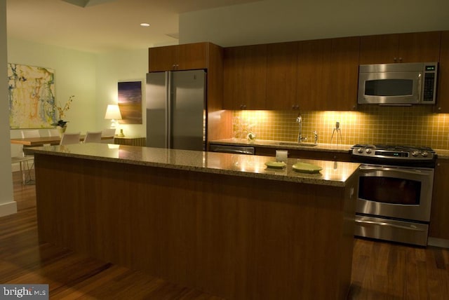 kitchen with dark wood-style flooring, light stone countertops, appliances with stainless steel finishes, and a sink