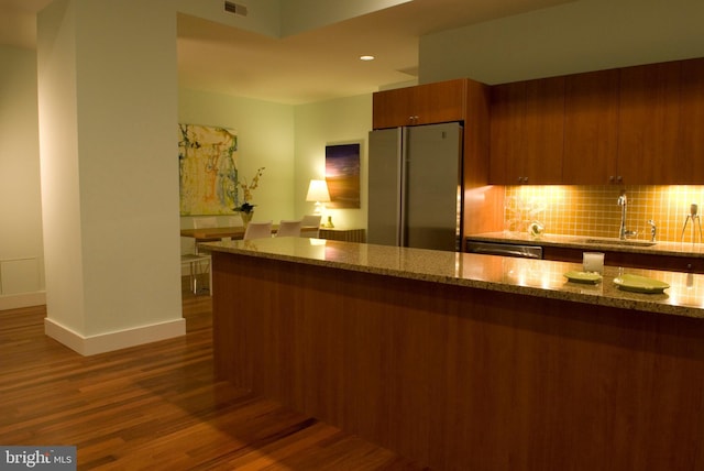 kitchen with a sink, stainless steel appliances, dark wood finished floors, baseboards, and backsplash