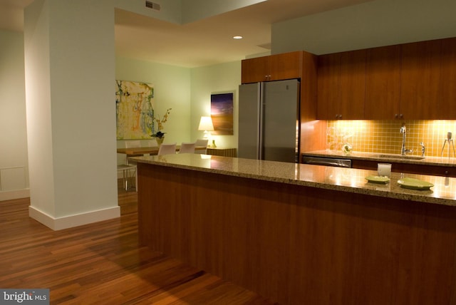 kitchen featuring a sink, decorative backsplash, wood finished floors, brown cabinets, and stainless steel appliances