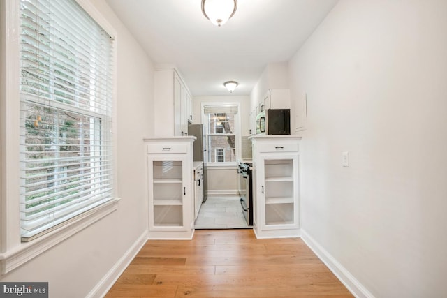 corridor with healthy amount of natural light, baseboards, and light wood-type flooring