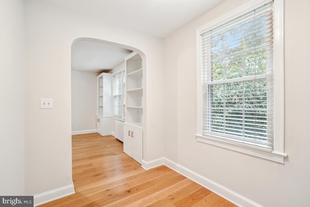 hall featuring baseboards, plenty of natural light, light wood-type flooring, and arched walkways