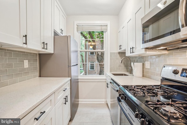 kitchen with stainless steel appliances, a sink, white cabinets, baseboards, and tasteful backsplash