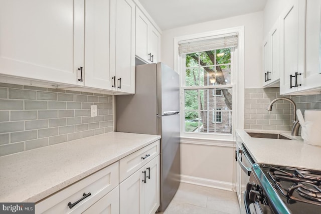 kitchen featuring gas range oven, a sink, white cabinetry, baseboards, and light stone countertops