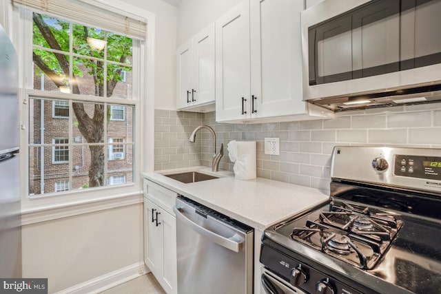 kitchen featuring appliances with stainless steel finishes, a sink, white cabinetry, backsplash, and baseboards