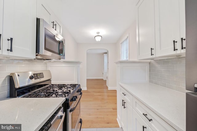 kitchen with stainless steel appliances, arched walkways, light wood-style floors, and white cabinets