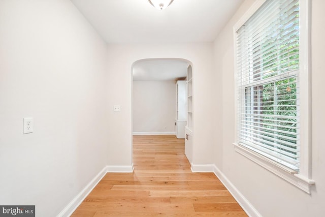 hallway with arched walkways, light wood-style floors, and baseboards