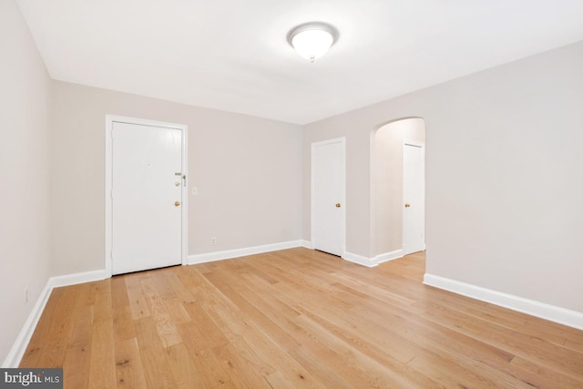 spare room featuring arched walkways, light wood-style floors, and baseboards