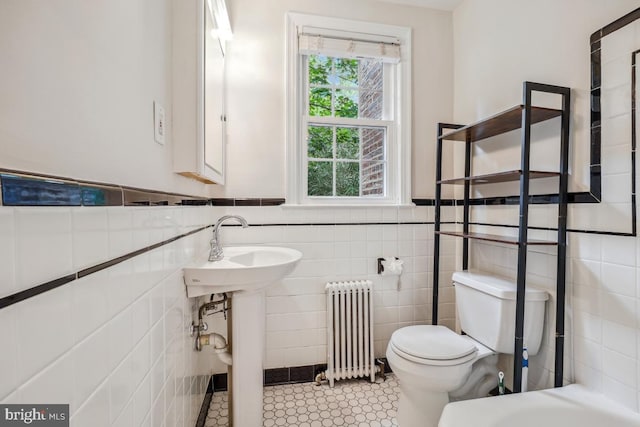 bathroom featuring radiator, toilet, tile walls, and a wainscoted wall