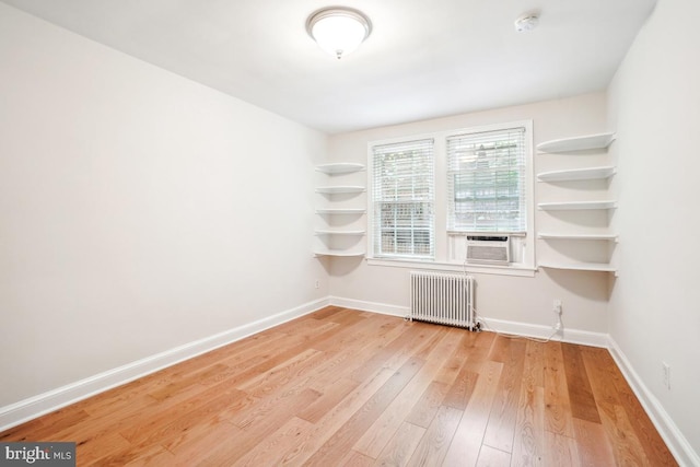 empty room with radiator, light wood finished floors, baseboards, and a smoke detector