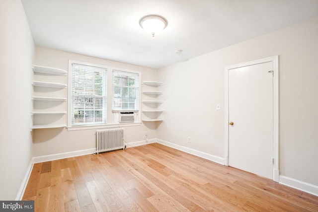 spare room featuring radiator, wood finished floors, baseboards, and cooling unit