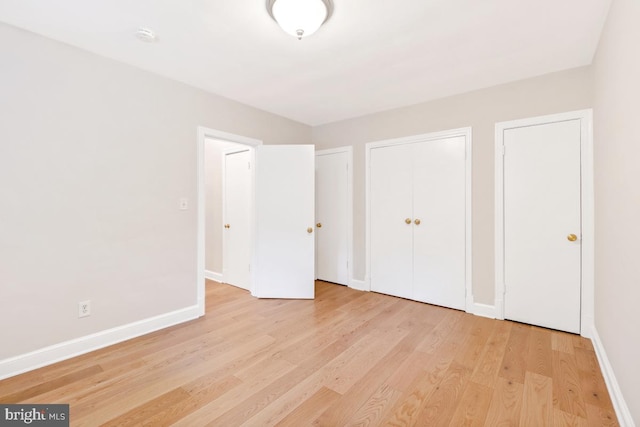 unfurnished bedroom with baseboards, light wood-style floors, and multiple closets