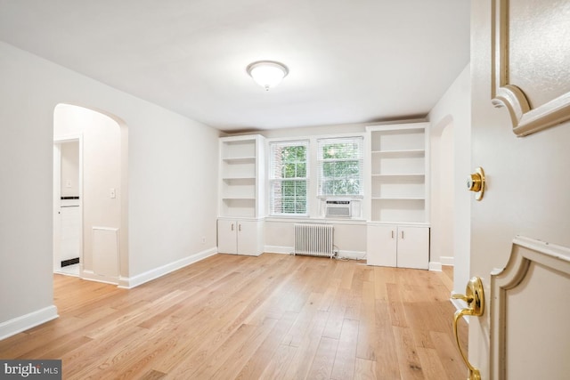 empty room with radiator heating unit, arched walkways, light wood-style flooring, cooling unit, and baseboards