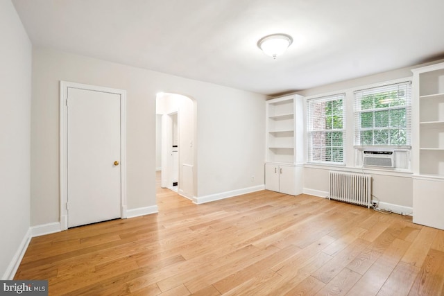 empty room featuring radiator heating unit, arched walkways, light wood-type flooring, and baseboards