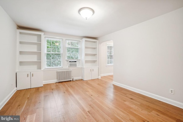 unfurnished room featuring radiator, arched walkways, light wood-style floors, and baseboards