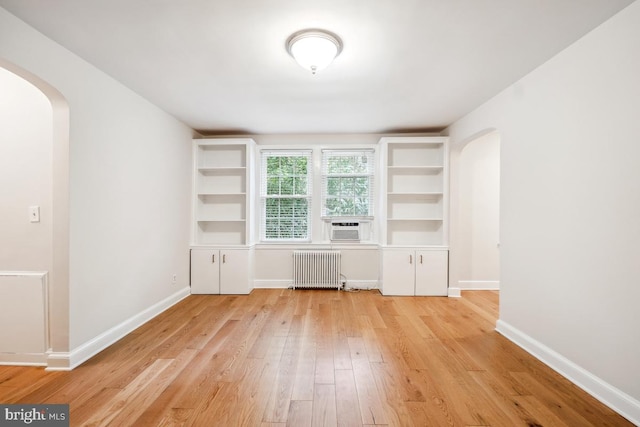 unfurnished room with arched walkways, radiator heating unit, light wood finished floors, baseboards, and cooling unit
