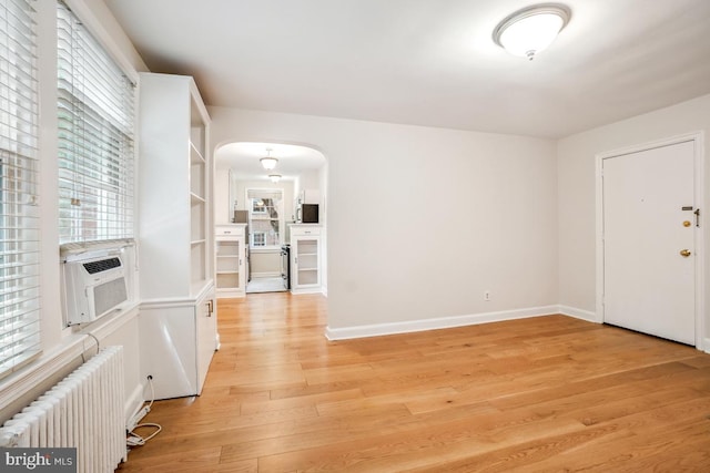 entryway featuring radiator heating unit, light wood-style floors, arched walkways, cooling unit, and baseboards