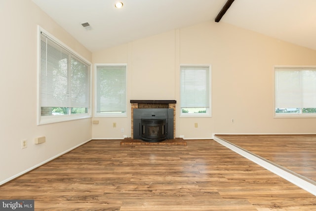 unfurnished living room featuring a wood stove, visible vents, wood finished floors, and lofted ceiling with beams