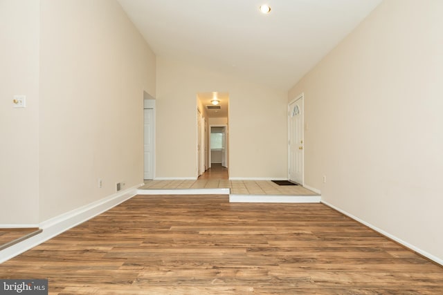 spare room featuring baseboards, wood finished floors, and vaulted ceiling