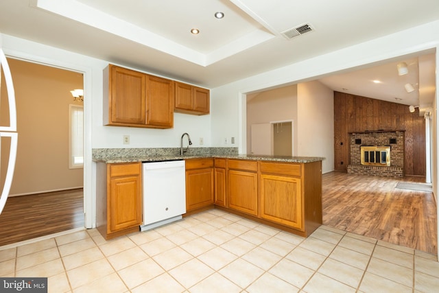 kitchen with a sink, light wood-type flooring, dishwasher, a brick fireplace, and light stone countertops