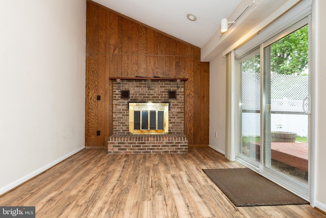 unfurnished living room with wood finished floors, vaulted ceiling, a fireplace, wooden walls, and baseboards